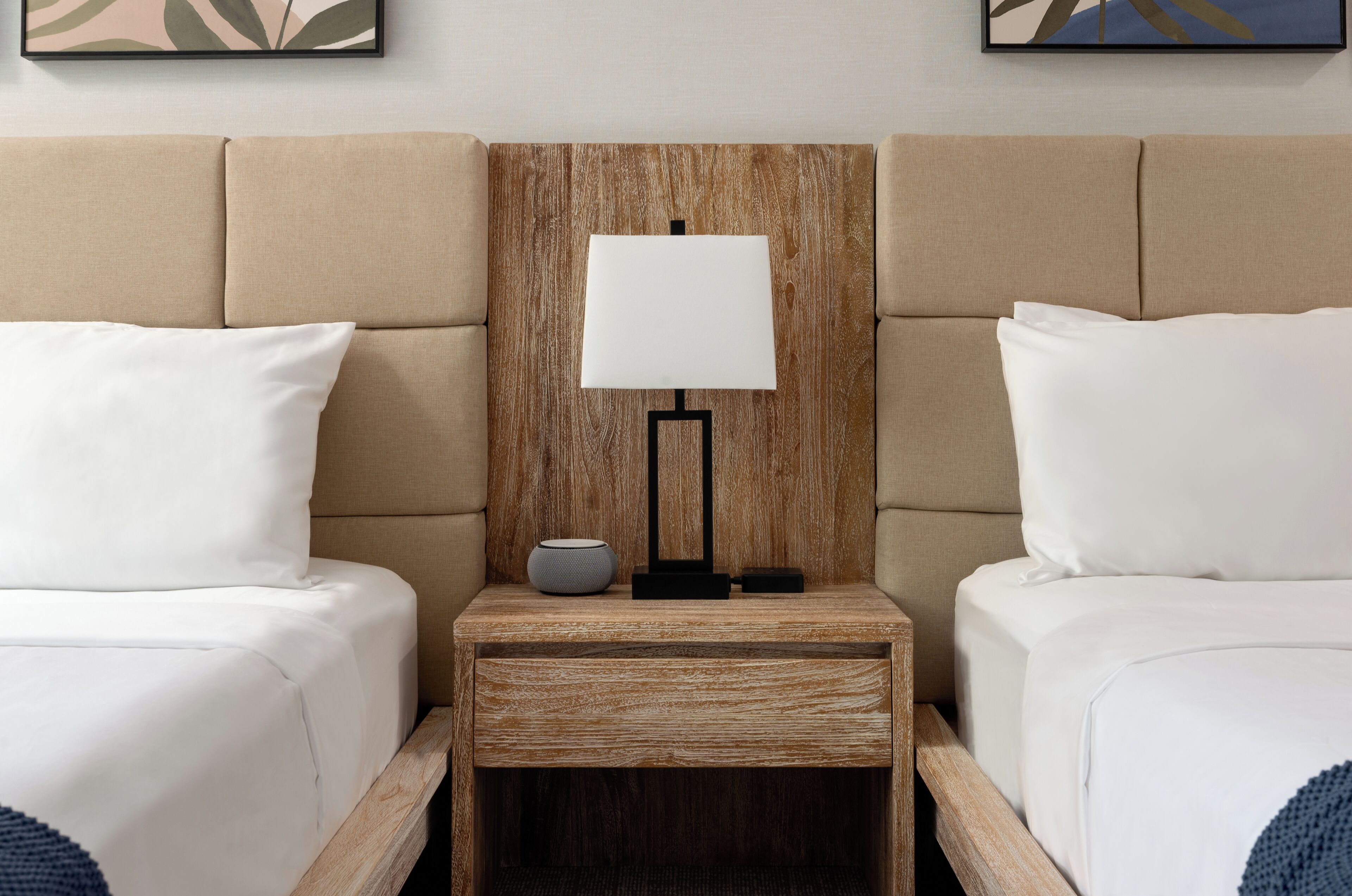 A hotel room with two beds, a wooden nightstand with a lamp, and a small table with a bowl.