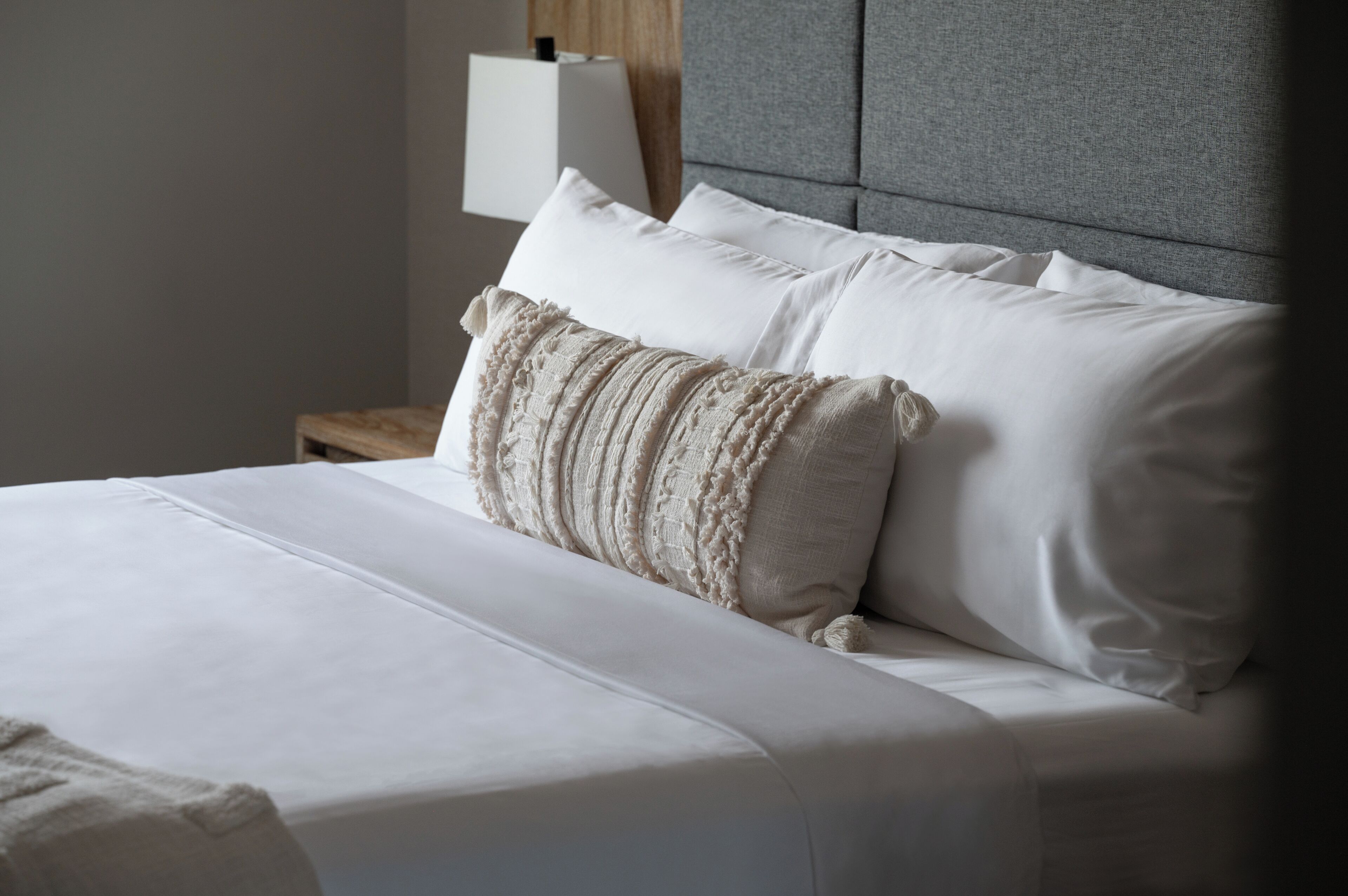Een net opgemaakt bed met witte lakens en een gebreid plaids.
