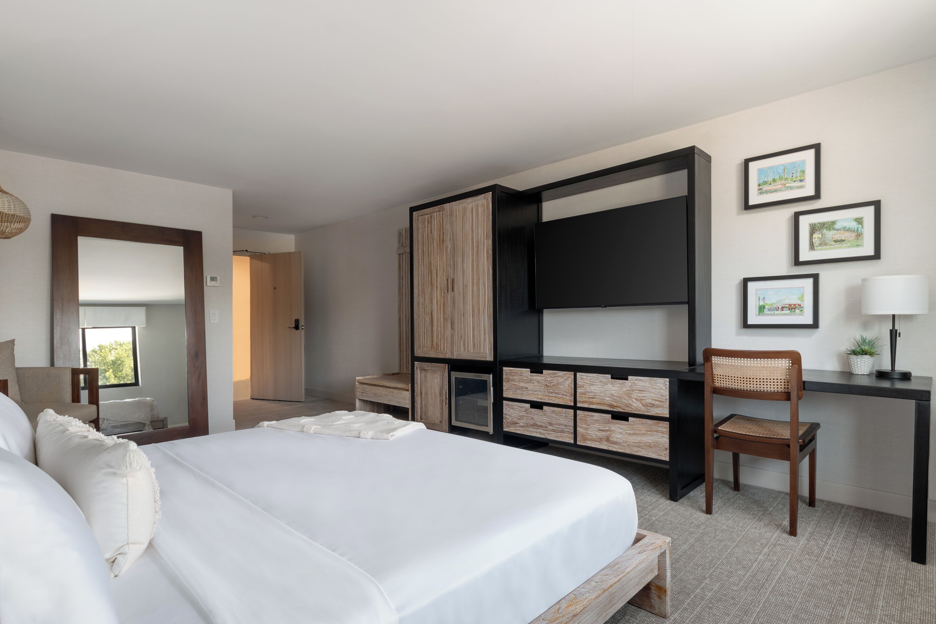 Een hotelkamer met een groot bed, een bureau met stoel, een televisie en ingelijste foto’s aan de muur.