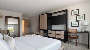 A hotel room with a large bed, a desk with a chair, a television, and framed pictures on the wall.