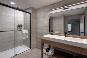 A modern bathroom with a glass-enclosed shower, a wooden vanity with a sink, and a large mirror. - The Wave at Marblehead (Marblehead)