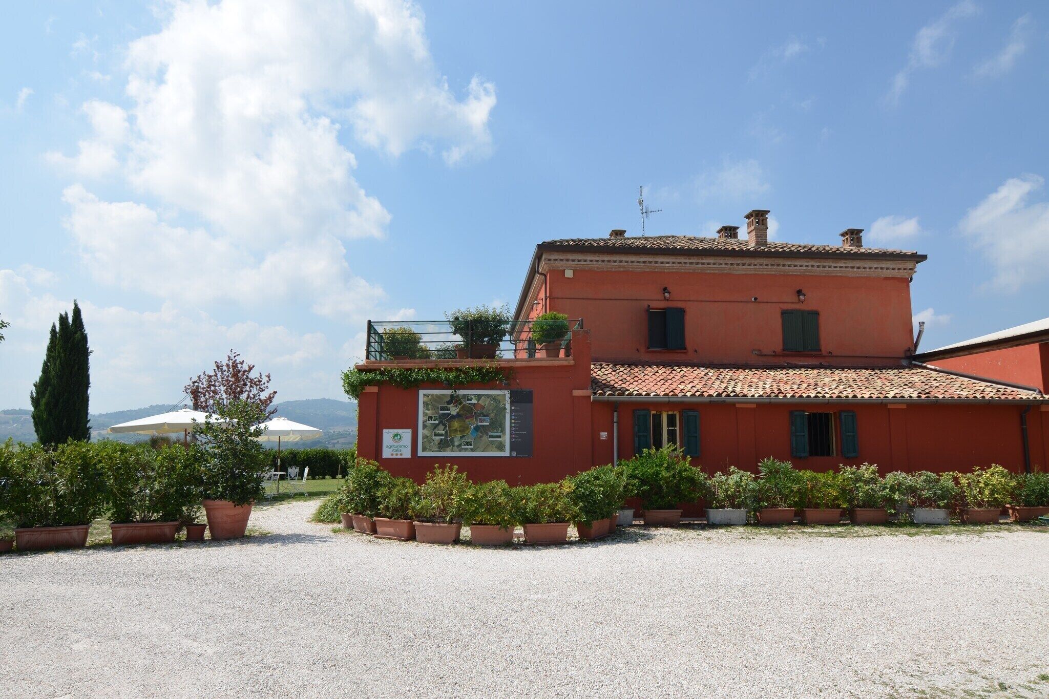 A red building with a tiled roof, surrounded by potted plants and a gravel path.