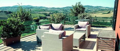 A terrace with wicker furniture, a potted plant, and a view of rolling hills.