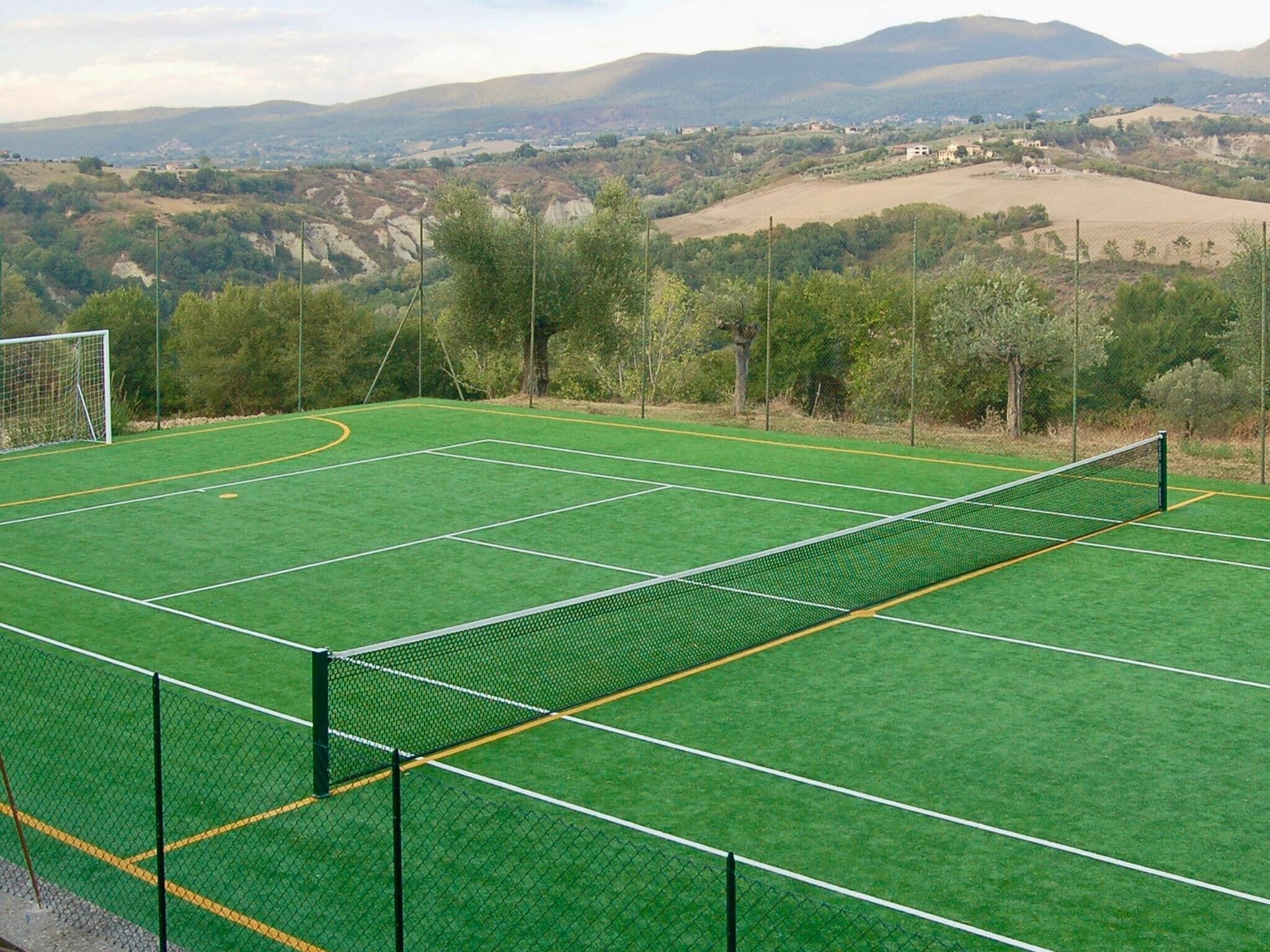 Ein Tennisplatz mit Netz, umgeben von Bäumen und Hügeln im Hintergrund.
