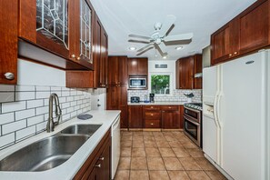 A kitchen with wooden cabinets, a stainless steel sink, a microwave, a stove, and a ceiling fan.