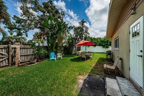 A backyard with a wooden fence, a dining table with chairs, a red umbrella, and a potted plant.
