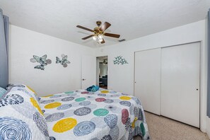 A bedroom with a bed, a ceiling fan, and butterfly wall decals.