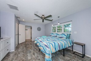 A bedroom with a bed, a ceiling fan, a window, and a door.