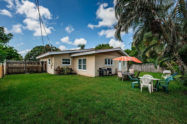 A residential backyard with a house, a wooden fence, and a patio area with outdoor furniture.