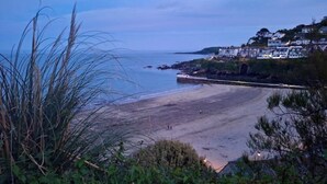 A coastal beach with a curved shoreline, a pier extending into the water, and residential buildings on a hillside. - Cliff Face in Living Room! Beach 1 Min. Looe (Looe)
