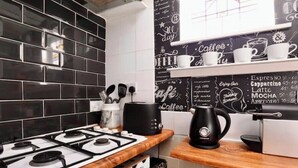 A kitchen with black tiled backsplash, a coffee station, and a gas stove. - Cliff Face in Living Room! Beach 1 Min. Looe (Looe)