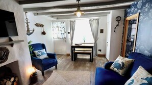 A cozy living room with a blue sofa, a fireplace, and a dining area with a table and chairs. - Cliff Face in Living Room! Beach 1 Min. Looe (Looe)