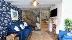 A living room with a blue sofa, a wooden coffee table, a stone wall, a fireplace, and a staircase leading to an upper level. - Cliff Face in Living Room! Beach 1 Min. Looe (Looe)