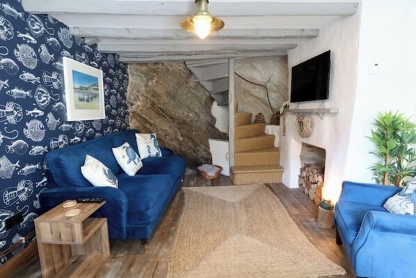 Ein Wohnzimmer mit blauem Sofa, Holztisch, Steinwand, Kamin und einer Treppe, die in eine obere Ebene führt.