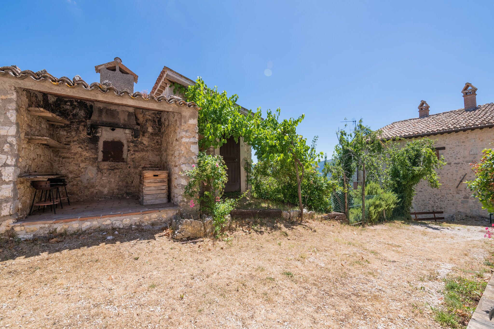 A rustic stone building with a tiled roof, a small wooden table, and a bench.