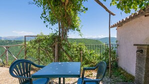 A rustic outdoor seating area with a table and chairs, surrounded by greenery and a view of distant hills. - Holiday Home in Sellano with Pool & Sun Terrace (Sellano)