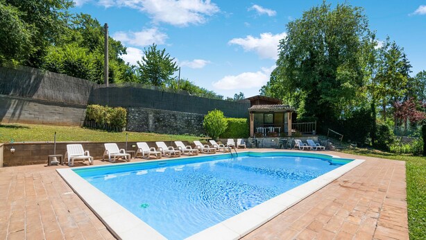 A rectangular swimming pool with a tiled deck, surrounded by white lounge chairs and a covered seating area.