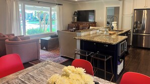 A modern kitchen with a central island, stainless steel appliances, and a dining area with a red chair and a table. - Charming Ranch - Near it All in East Dallas! (Dallas)