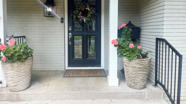 A front door with a black door and a wreath, flanked by two large planters with flowers, a mailbox, and a lantern on the wall. - Charming Ranch - Near it All in East Dallas! (Dallas)