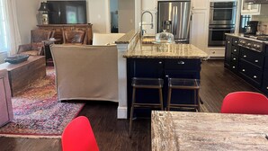 A modern kitchen with stainless steel appliances, a marble countertop, and a dining area with a red chair. - Charming Ranch - Near it All in East Dallas! (Dallas)