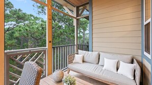 A balcony with a sofa and a wicker chair, overlooking a forested area. - New List 3BR/2BA Golf Cart - 6 seater Walk to Beach Top of the Dune (Santa Rosa Beach)