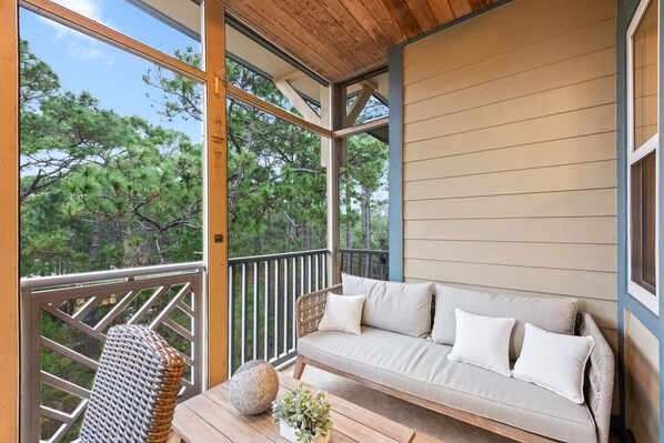 A balcony with a sofa and a wicker chair, overlooking a forested area.