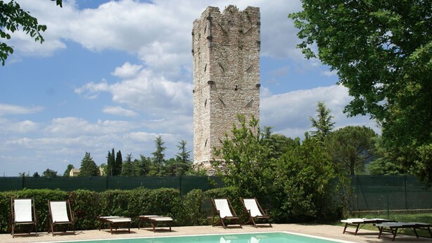 A swimming pool with lounge chairs and a stone tower in the background.