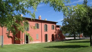 A red building with green shutters, a well-maintained lawn, and a tree in the foreground.