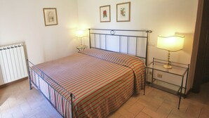 A bedroom with a bed, two bedside tables with lamps, a radiator, and two framed pictures on the wall.