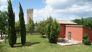 A courtyard with a red building, a stone tower, and tall cypress trees.