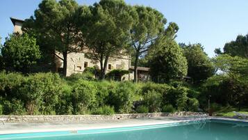 A pool area with a stone building in the background, surrounded by trees and greenery.