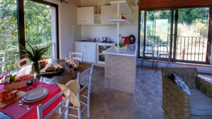 A modern kitchen with white cabinets, a dining area with a red table, and a balcony with wicker furniture. - Holiday home with pool near Assisi (Assisi)