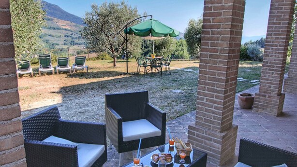 An outdoor patio with wicker furniture, a table set with food and drinks, and a view of the countryside. - Holiday home with pool near Assisi (Assisi)