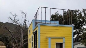Un piccolo edificio giallo e blu con una scala che conduce a una porta.
