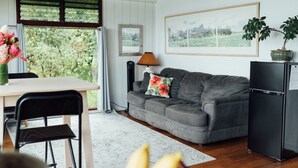 Una habitación con techo de madera, un sofá gris, un refrigerador negro y un área de comedor con mesa y sillas.