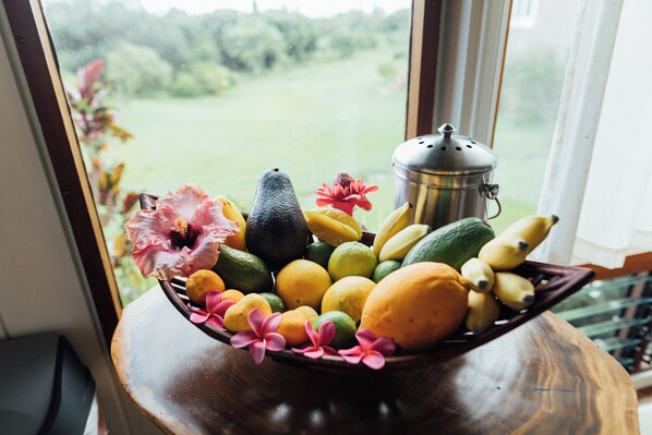 A wooden bowl filled with fruits and flowers on a table by a window.