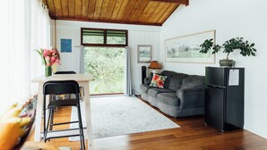 Un espacio habitable compacto con techo de madera, una zona de comedor con mesa y sillas, un sofá, un refrigerador negro y una ventana con vistas a zonas verdes.