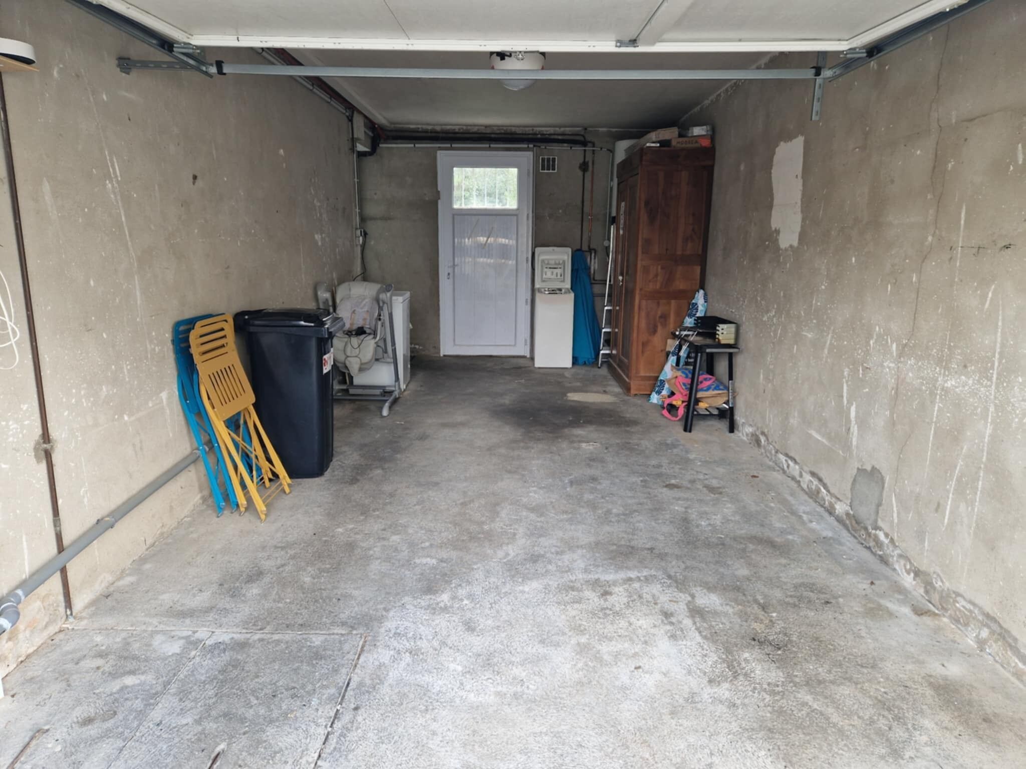 A garage with a concrete floor, a white door, and a wooden cabinet.