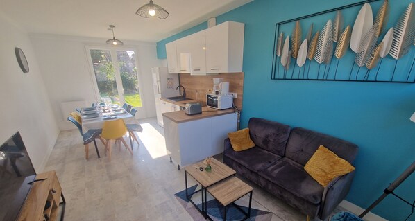 Un salon moderne avec un canapé foncé, une table basse et un coin repas comprenant des chaises et une table.