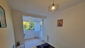 Et soveværelse med en seng, et lille natbord, en lampe og udsigt til det fri gennem et vindue.