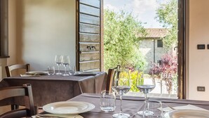 Un coin repas avec une table dressée pour quatre personnes, une porte en bois et une vue sur un jardin et un bâtiment à l’extérieur.