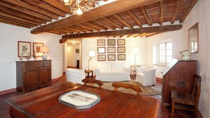 A spacious living room with a wooden dining table, white sofas, and a chandelier.