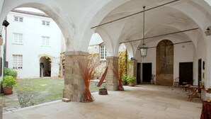 A courtyard with arches, stone flooring, potted plants, and a hanging light fixture.