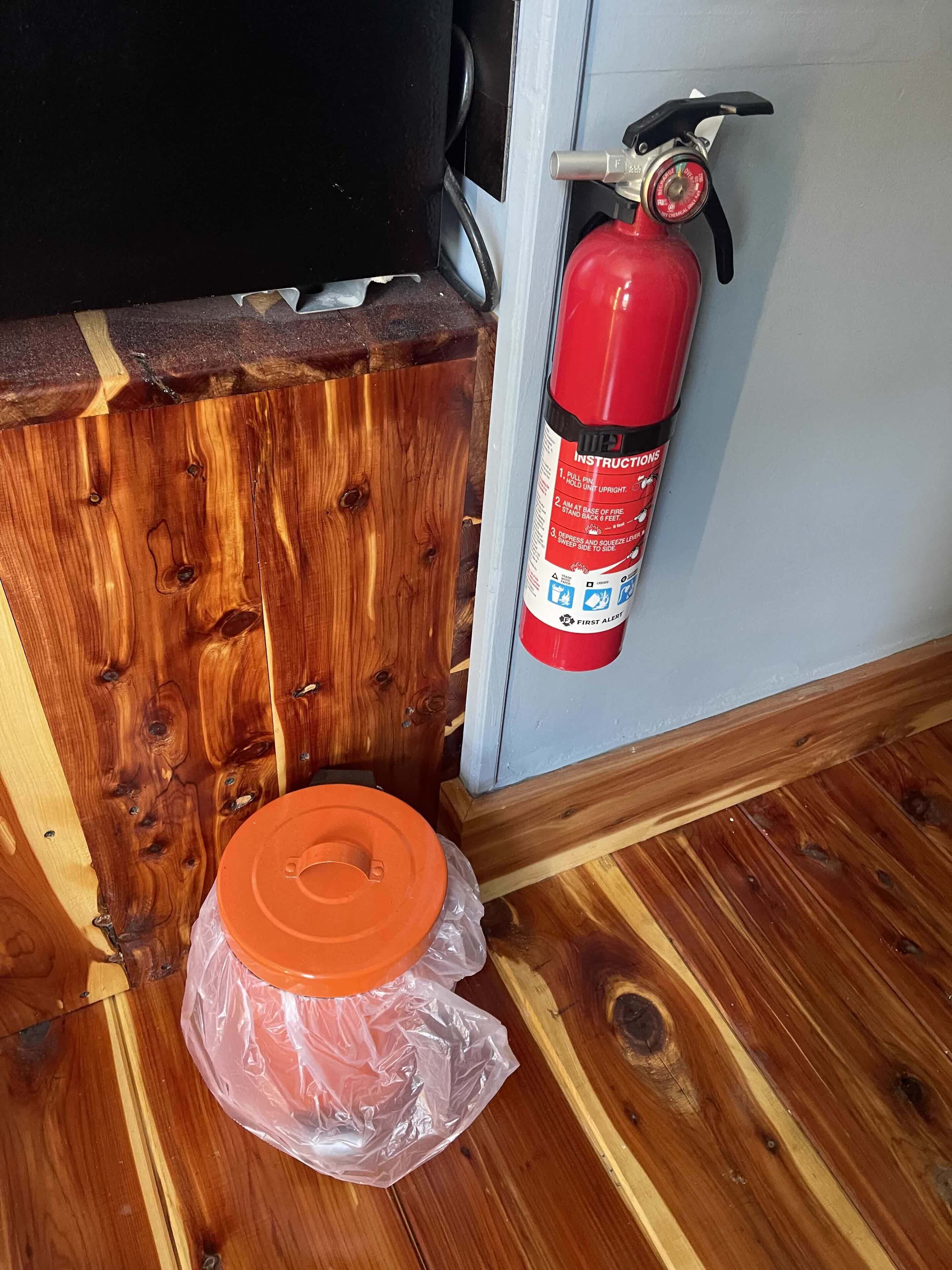 A wooden floor with a plastic container and a fire extinguisher mounted on a wall.