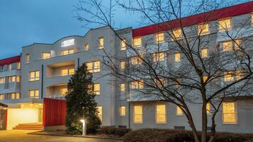 Ein mehrstöckiges Hotel mit schlichter Fassade, Balkonen und einem roten Akzent am Dach.