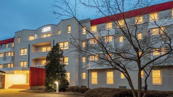 A multi-story hotel with a flat facade, balconies, and a red accent on the roof.
