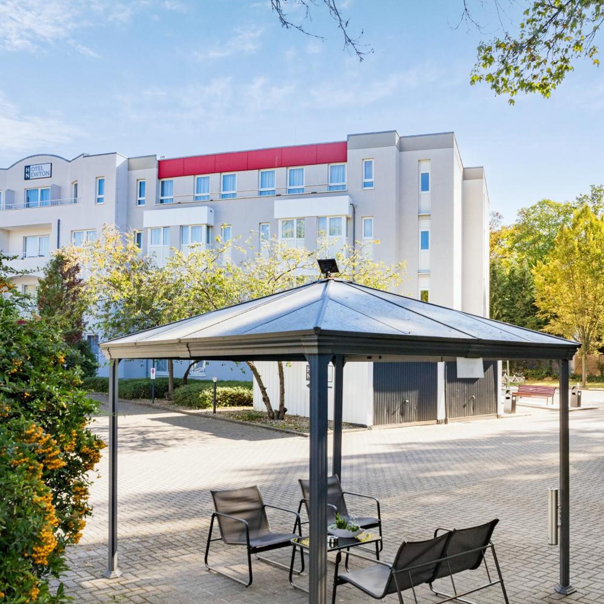 Ein modernes Hotel mit einer überdachten Außenbereich-Sitzgelegenheit, einem roten Markisenvorbau und freiem Blick auf die Vorderseite des Gebäudes.