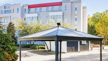 Ein modernes Hotel mit einer überdachten Außenbereich-Sitzgelegenheit, einem roten Markisenvorbau und freiem Blick auf die Vorderseite des Gebäudes.