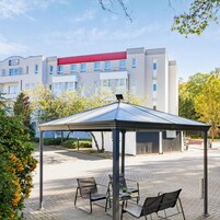 Un hotel moderno con un área de estar exterior cubierta, un toldo rojo y una vista despejada de la fachada del edificio.