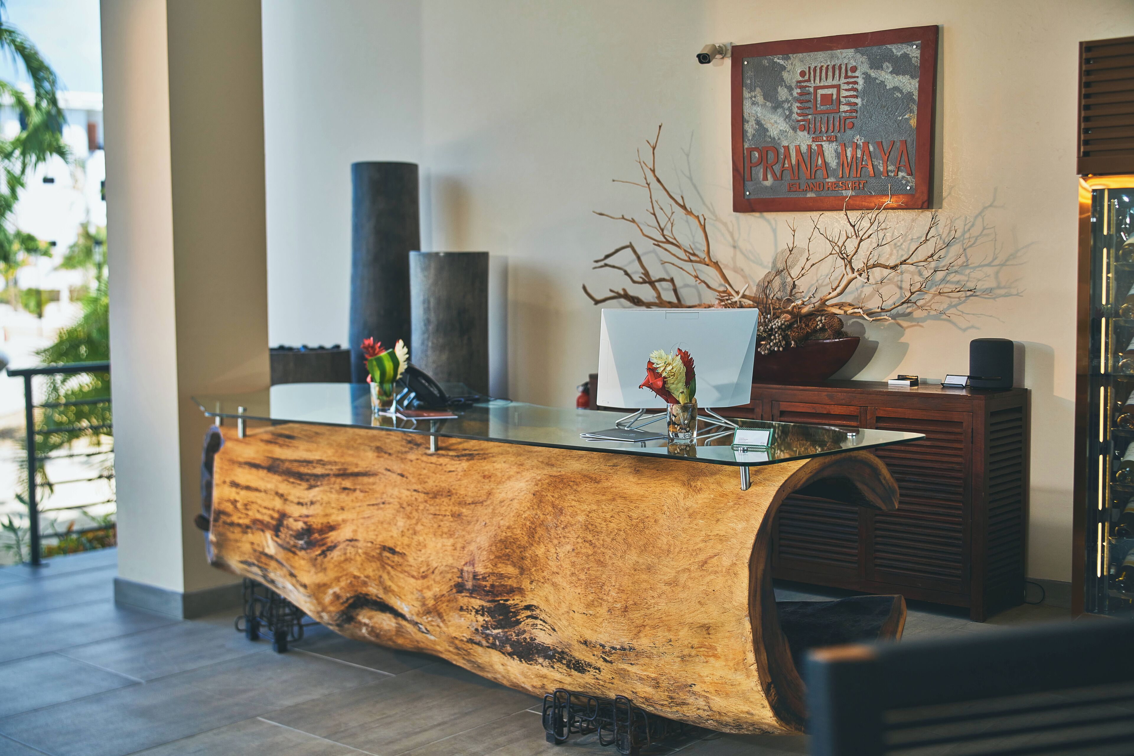 Una recepción con un mostrador de madera grande, una planta en maceta y un letrero que dice 'PRANA MAYA LAND RESORT'.